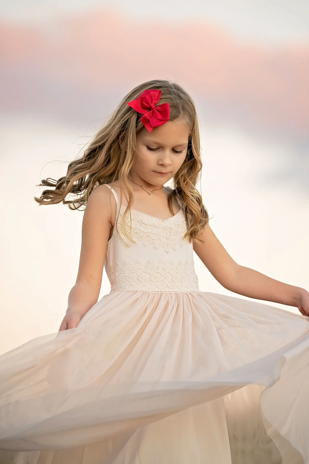 A girl twirling her dress beside the water at sunset