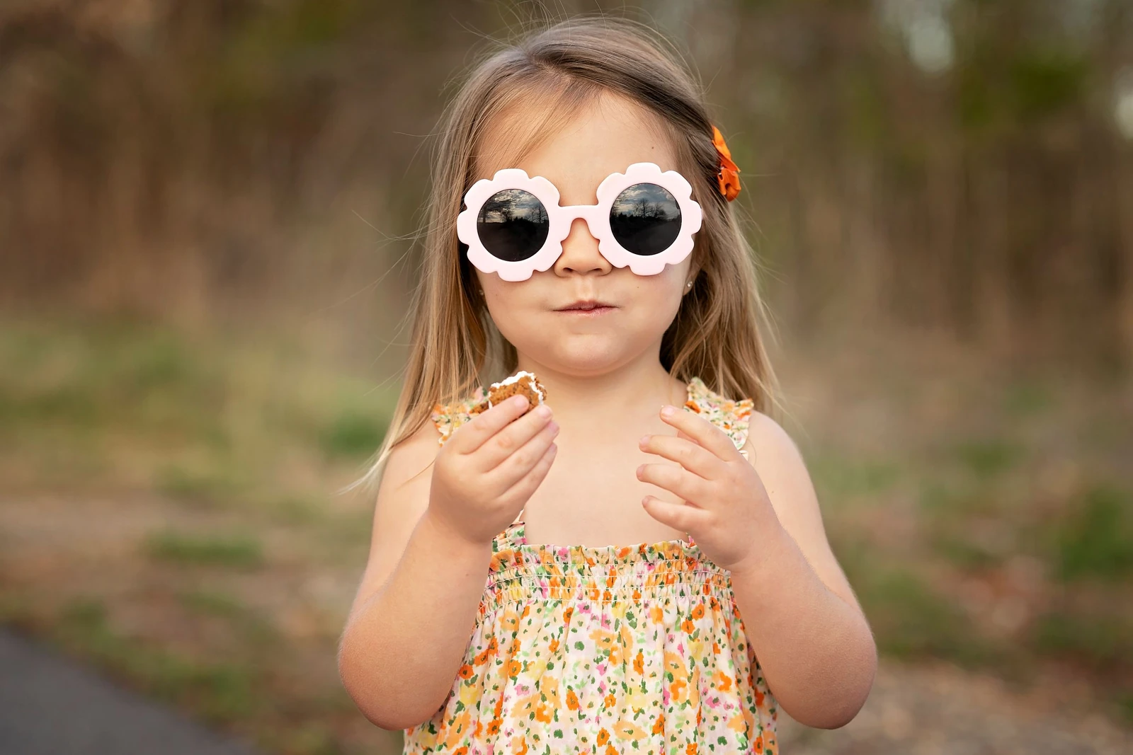 A little girl in flower-shaped sunglasses enjoying a snack in the sunshine