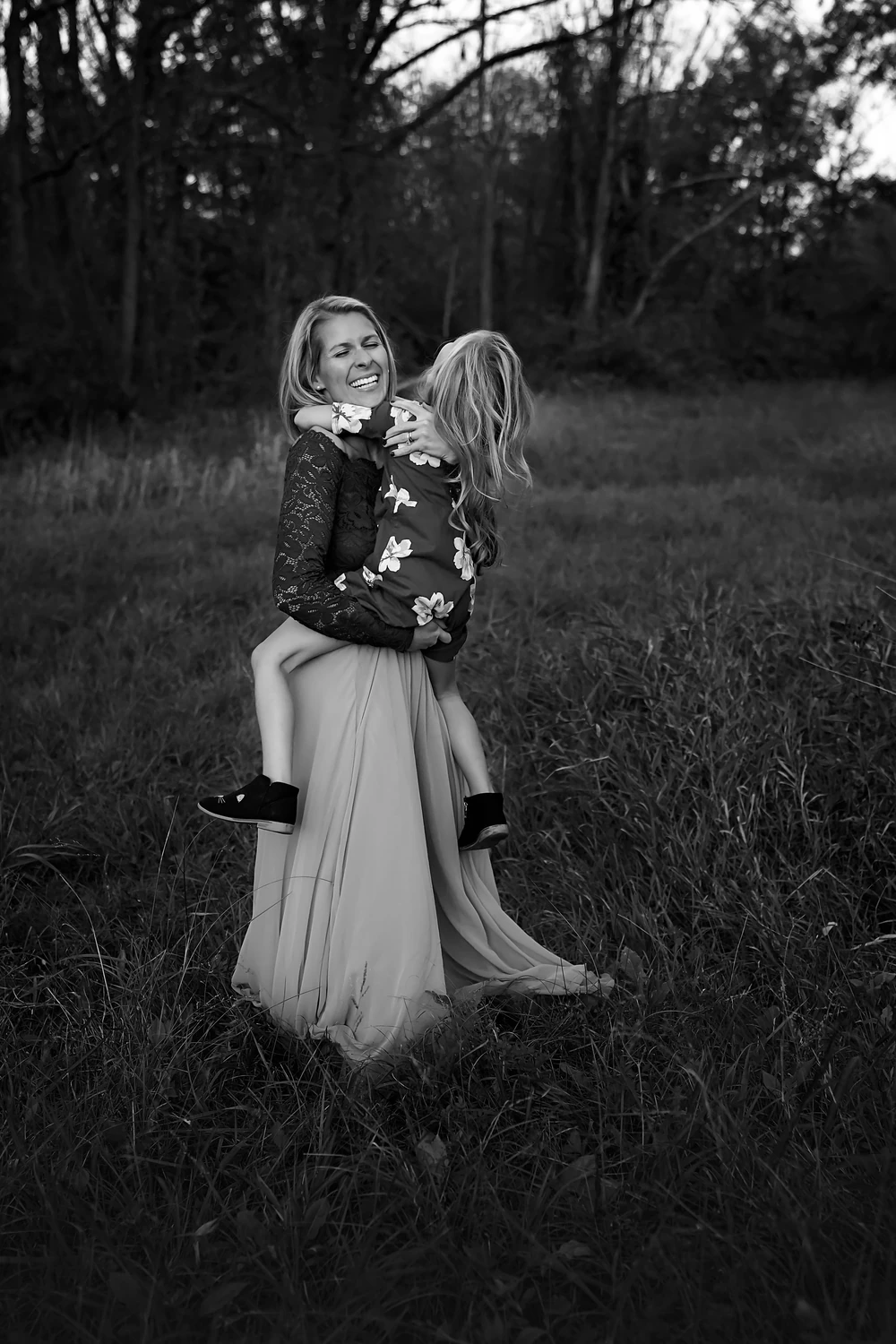 Erica smiling while holding her daughter in a field, in black and white