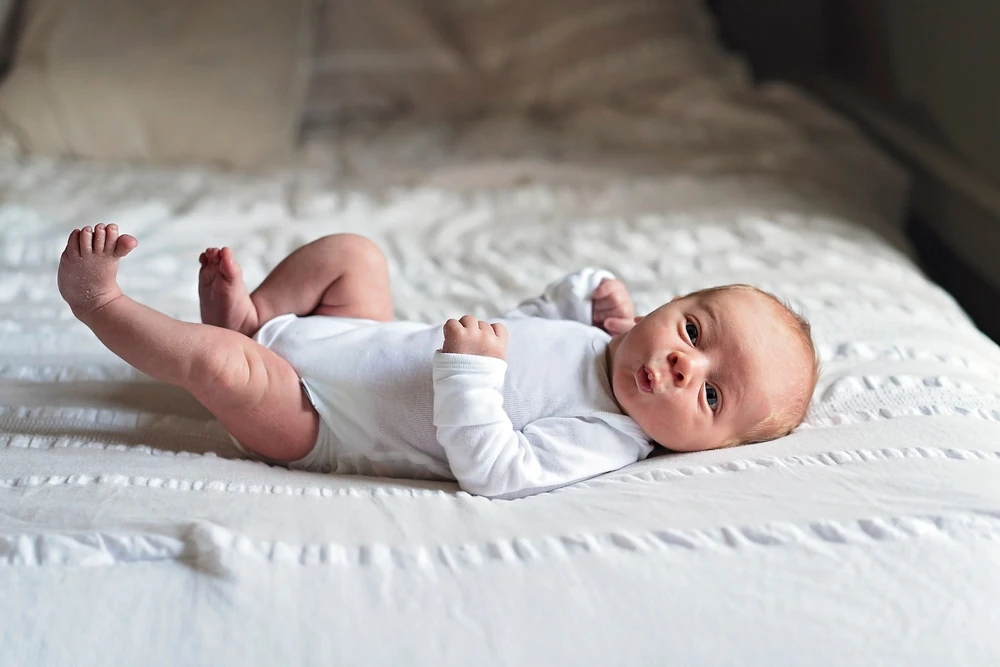 A wide-eyed newborn resting on a quilt at home