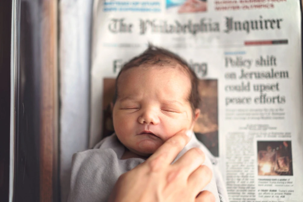 A sleeping newborn beside the day’s newspaper